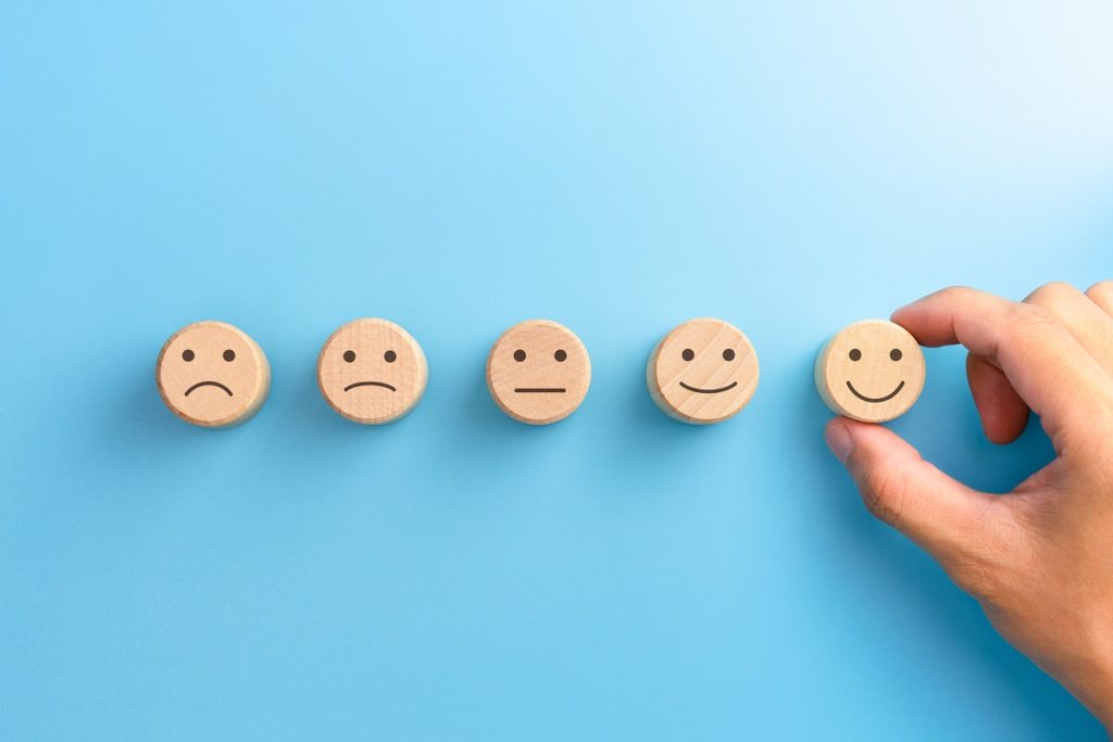 Customer service evaluation and satisfaction survey concepts. The client’s hand picked the happy face smile face icon on wooden cube on blue background. copy space