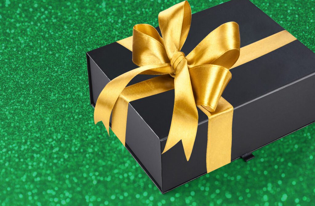 Black box wrapped with gold bow on sparkly green background