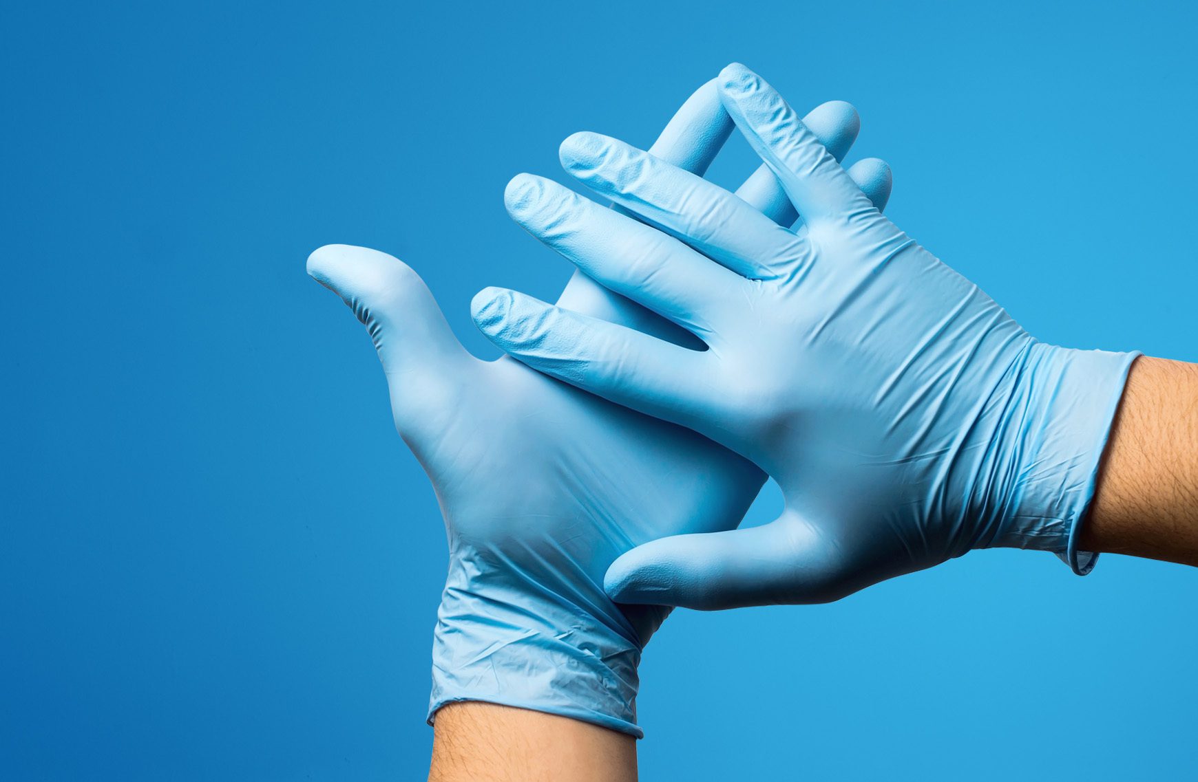 Hands wearing nitrile vinyl gloves against plain blue background